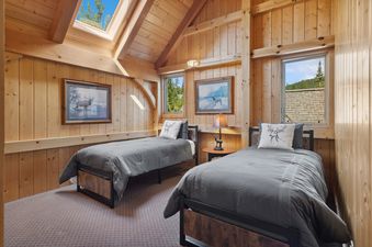 A cozy guest bedroom at Rested Ridge Ski Haus with two twin beds, wood-paneled walls, and a skylight.