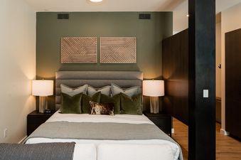 A serene bedroom at 230 LakeLodge with a plush bed, olive green accent wall, and elegant decor.