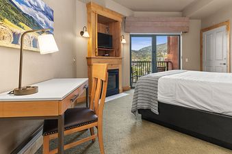 The Steamboat Grand Deluxe King features a cozy bedroom with a comfortable king-size bed, a functional desk with a lamp, and a charming fireplace.