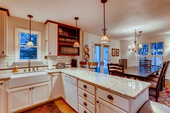 The interior of Chalet Montagne showcasing the kitchen area with white cabinetry, granite countertops, and an open dining space with a dark wood table and chairs.