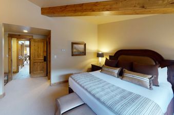 The king-size bed has white linens, a striped comforter, and brown pillows. There is a small table beside the bed with a lamp on it.
