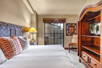 A cozy bedroom at Copperbottom 307 features a large bed with white linens, a decorative headboard, and an antique wooden armoire with a TV.