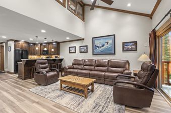 A wide view of the open-concept living room and kitchen in Snow Flower 71 Park City, featuring brown leather furniture, a wooden coffee table, and a modern kitchen with dark wood cabinets.