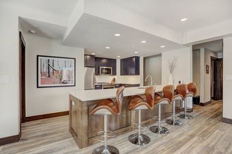 A kitchen island with four bar stools in a modern kitchen with light wood floors, white quartz countertops, and dark blue cabinets.