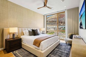 The bedroom at Founders Place 2502 features a large bed with white linens, a wooden ceiling fan, and expansive windows offering views of autumn hillsides.