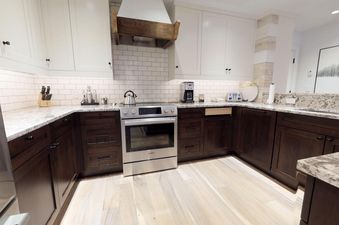 A modern kitchen with white upper cabinets, dark wood lower cabinets, and light granite countertops, featuring a stainless steel stove and hood.
