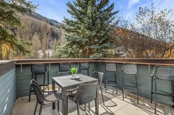 A private balcony at Seven Summits with a black dining table and chairs, along with high-top bar stools, overlooks a vibrant autumn mountain landscape.