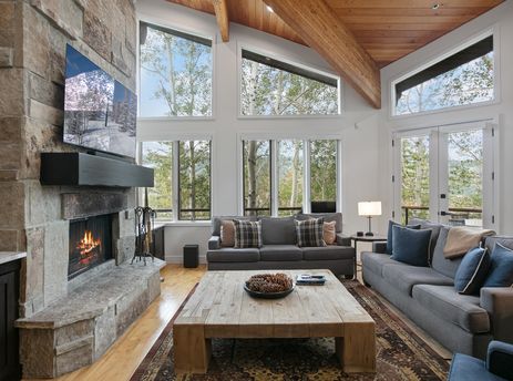 Bright and spacious living room at Twin Pines 5 featuring a large stone fireplace, cozy sofas, and high windows with nature views.