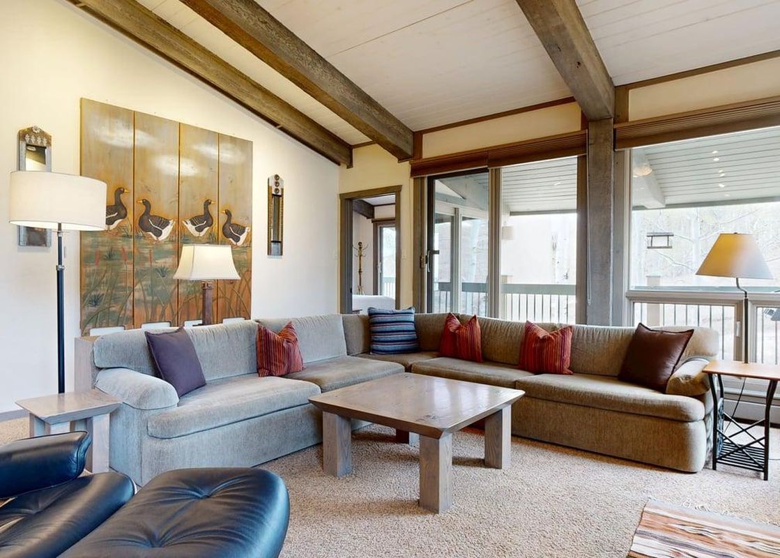 The comfortable and elegantly furnished living area at Top of the Village Leaf 503, featuring a large sectional sofa, wooden coffee table, and an artwork depicting ducks, all set under vaulted ceilings with exposed beams.