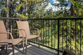 The balcony at Vasquez Creek Townhomes 8 features two chairs, a dark railing, and a view of many evergreen trees.