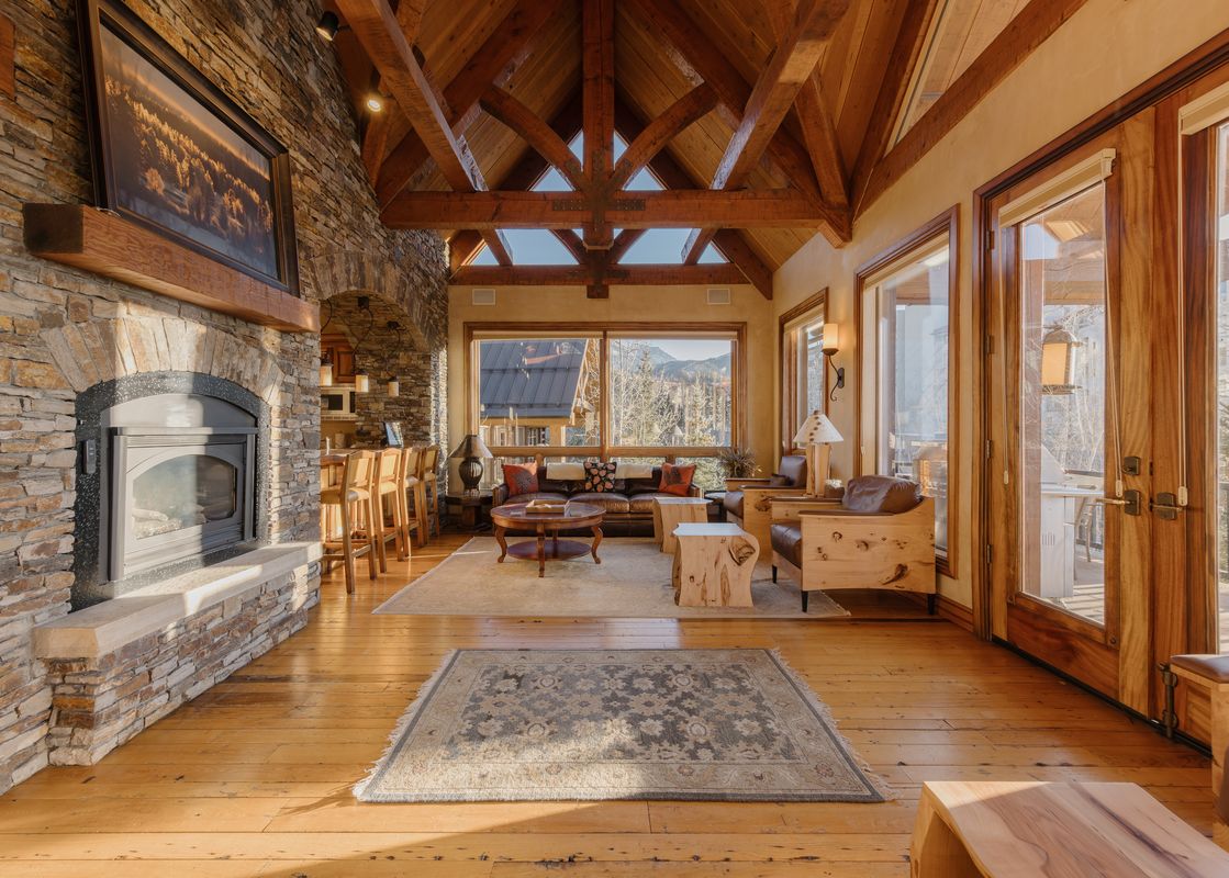 The great room at Palmyra Vista Cabin at See Forever features a vaulted wooden ceiling, a large stone fireplace, and expansive windows with mountain views.