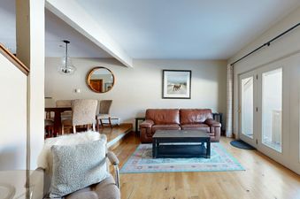The living area of The Fairway Serenity features a comfortable brown leather couch, a coffee table, a throw rug, and an entry to a patio.