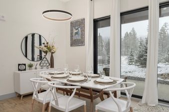 The dining area in Timber Fox B 2102 features a white dining table set with place settings, surrounded by white chairs, under a modern circular chandelier.