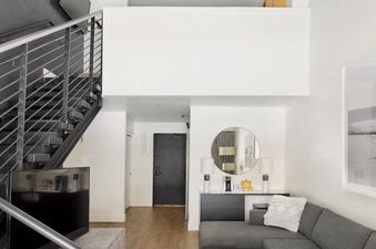 The living room of the Gravity Haus JH Loft featuring a gray sectional sofa and a metal staircase leading to the loft area.