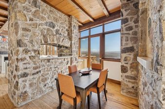 A rustic dining room at Snow Pine Lodge at Deer Valley featuring a wooden dining table, orange chairs, stone walls, and large windows with mountain views.