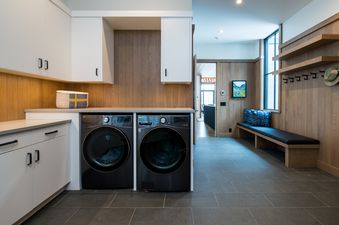 A modern laundry room with white cabinets, wood paneling, and a black washer and dryer