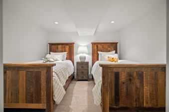 Two twin beds with wooden frames and striped bedding, separated by a nightstand with a lamp in a cozy bedroom.