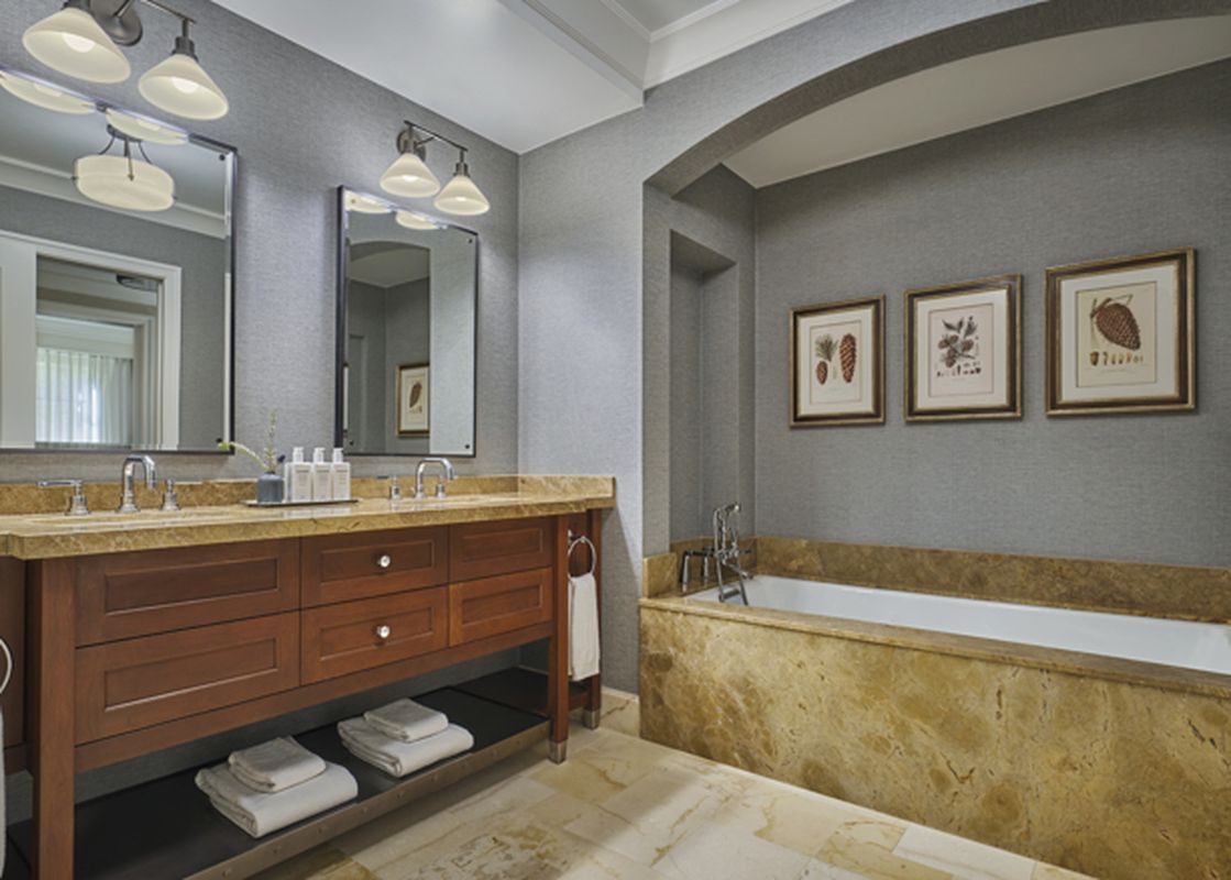 A modern bathroom features dual vanity sinks with dark wood cabinetry and a large marble-clad bathtub, illuminated by elegant sconces and recessed lighting.