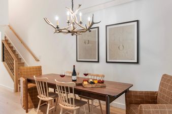 Elegant dining area at Cottonwood Jackson Hole featuring a wooden table, antler chandelier, and warm armchairs near a staircase.
