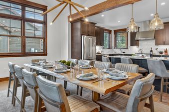 The spacious dining room and kitchen area of Cherrybrook Chalet, featuring a live-edge wooden dining table, modern gray chairs, and a contemporary sputnik chandelier.