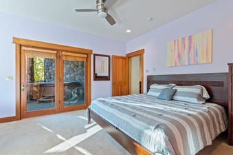 A comfortable bedroom at Ridge Top Chalet with a large bed, colorful abstract art, and glass doors leading to a patio with a hot tub.