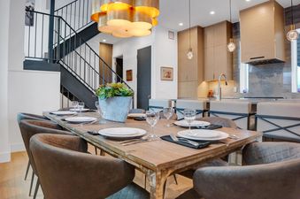 A modern dining area with a wooden table set for dinner and a contemporary kitchen with light wood cabinetry and marble backsplashes.