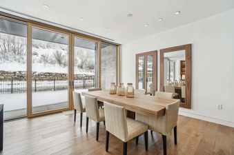 A modern dining room in Founders Place 2304 with a wooden table, upholstered chairs, and large glass doors revealing a snow-covered outdoor landscape.