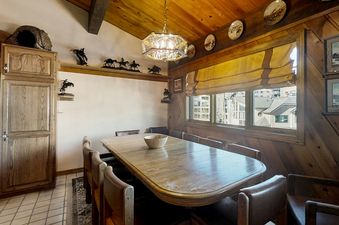 A close-up view of the dining area in Phoenix 216 shows the long wooden table and chairs, with a light fixture hanging overhead and wall decorations.