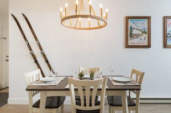A cozy dining area at River Street Refugio with a wooden table, place settings, a chandelier, vintage skis, and framed ski posters on the wall.