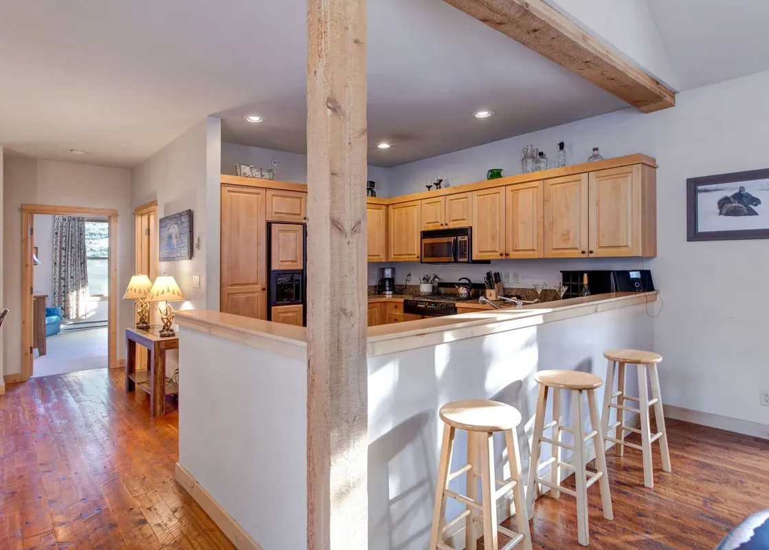 A modern kitchen with a breakfast bar featuring wood stools and a view into a hallway.