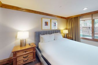 The bedroom at Manor Vail 118 features a king-size bed, nightstand, lamps, and a view out the window.
