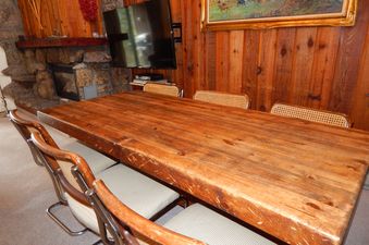 The dining area showcases a large wooden table with several chairs, a stone fireplace, and a wall-mounted television.