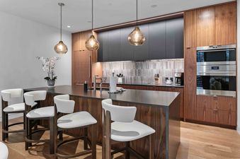 A modern, sleek kitchen in Founders 1402 with warm wood cabinetry, a dark island with barstools, and glowing pendant lights.