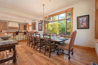 Dining area of Granite Ridge Lodge 6 with a long wooden table, high-backed chairs, and a large window looking out at autumn trees.