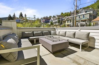 The outdoor living space at Parkite 34 features comfortable seating and a fire pit, set against a backdrop of distant houses and a clear blue sky.