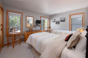 A cozy bedroom at Rendezvous A4 with two twin beds, rustic wood furniture, and windows with nature views.