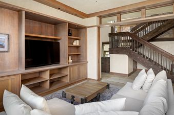 A spacious living room featuring a large wooden entertainment center with a television, a light-colored sectional sofa, and a rustic wooden coffee table.
