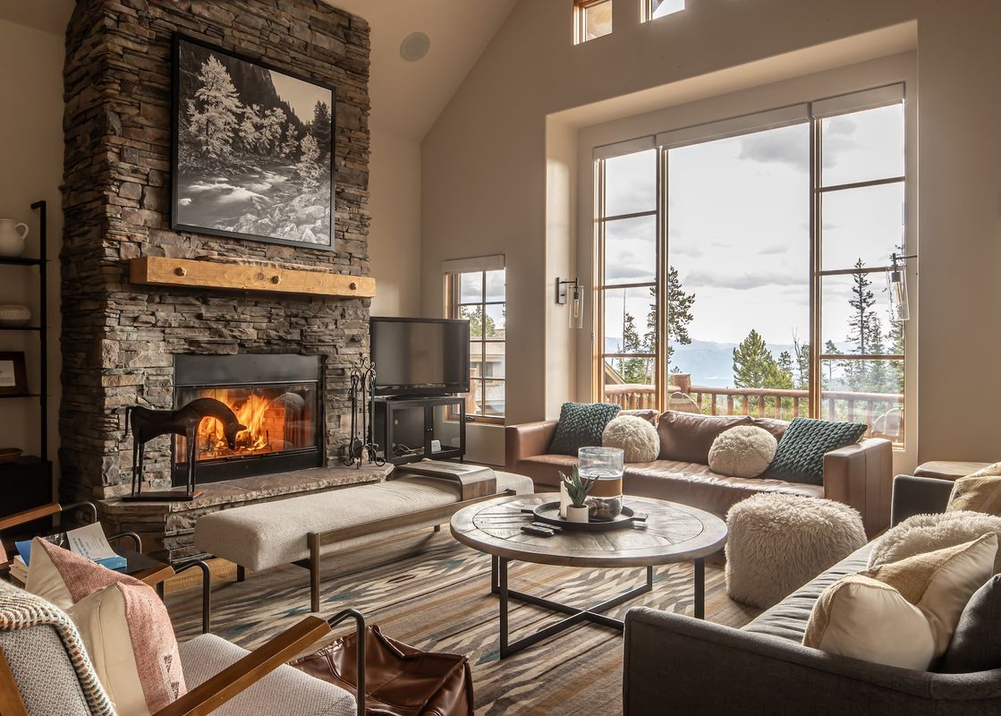 A spacious and inviting living room featuring a large stone fireplace, comfortable seating, and expansive windows offering stunning views of the outdoors.