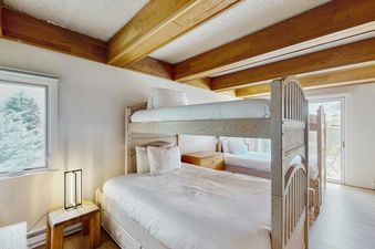 The bunk bedroom at Vail International 003 features a bunk bed with white linens, a nightstand, and a window overlooking snow-covered trees.