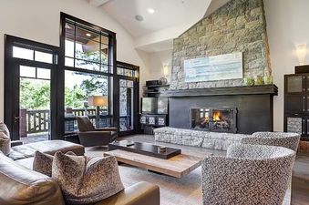 The living room of the Hummingbird Platinum 3 BR Plus Loft showcases a stone fireplace, large windows with outdoor views, and comfortable seating.