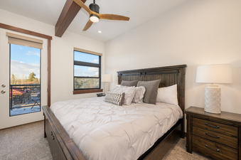 A master bedroom with a large bed, wooden furniture, and access to a balcony with views of the surrounding area.