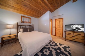 A cozy bedroom with a wooden bed frame, white bedding, and a light-colored rug, offering a comfortable and inviting atmosphere for guests.