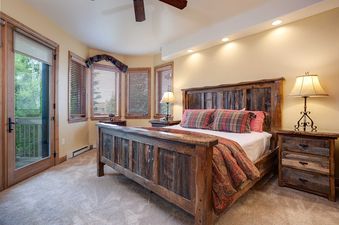 A master bedroom at Chateau Chamonix CX315 features a rustic wooden bed, warm lighting, and a door leading to a balcony.