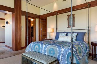 An elegant primary bedroom at Hale Hoaloha featuring a dark iron four-poster bed and warm wood accents.
