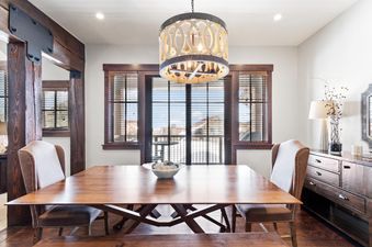 A sophisticated dining area at Silver Star 33 featuring a large wooden table, two upholstered chairs, and a bench, under a decorative drum-style chandelier, with large windows overlooking an exterior view.