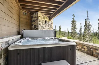 An outdoor hot tub under a wooden ceiling on a patio with mountain views.