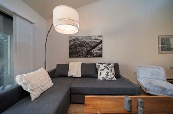 A cozy living room in Beaver Village 332 features a large gray sectional sofa, a tall arched floor lamp, and mountain artwork on the wall.