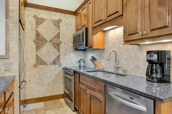 A modern kitchen with stainless steel appliances, dark granite countertops, and a mosaic tile backsplash featuring diamond patterns.