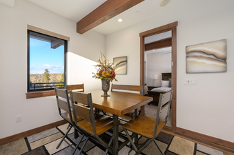 A cozy dining area featuring a wooden table and chairs, with a large window offering a view of the outdoors.
