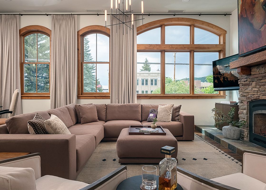 Cozy living room with a large brown sectional sofa, fireplace, and scenic arched windows at the 5th Street Penthouse.